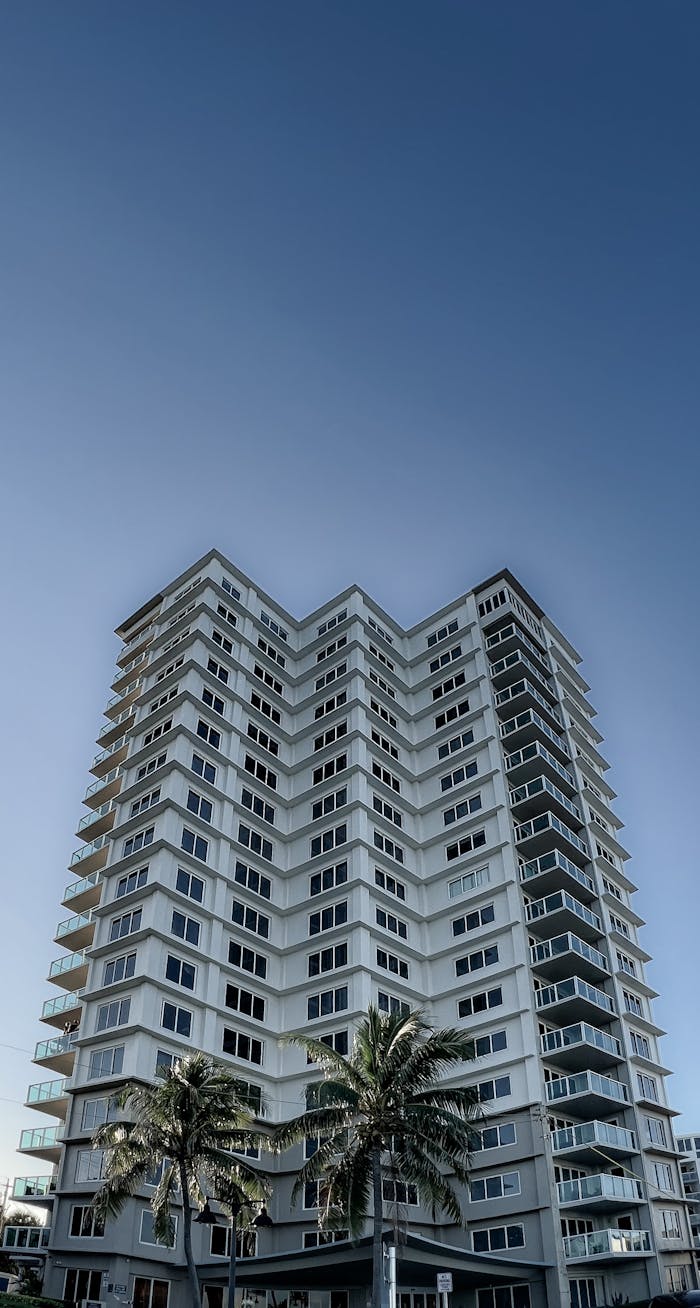 hero-img-02 Low-angle view of a tall condominium building under a clear blue sky.