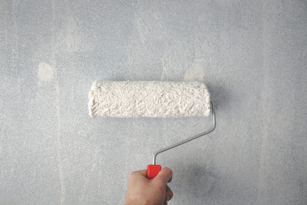 pexels-photo-1669754-1669754 A person's hand using a paint roller to apply white paint on a wall.